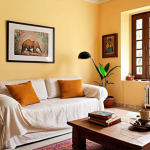 **

A cozy living room with light-colored walls, maximizing natural light.  Include a comfortable sofa, a small coffee table with Hindi books, and some plants to bring in natural elements.  The overall feeling should be airy and inviting, showcasing the use of light colors to make the space feel larger. Add some personal decorative items like photos or art that reflect Indian culture.

**
